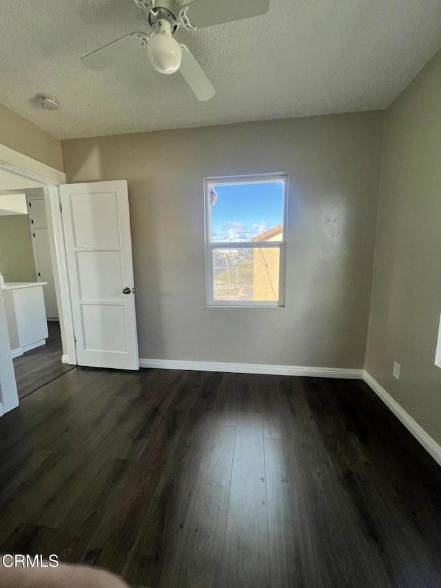 unfurnished bedroom featuring ceiling fan, baseboards, a textured ceiling, and dark wood finished floors