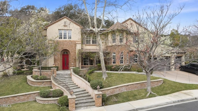 view of front facade featuring stucco siding, driveway, brick siding, and a front yard