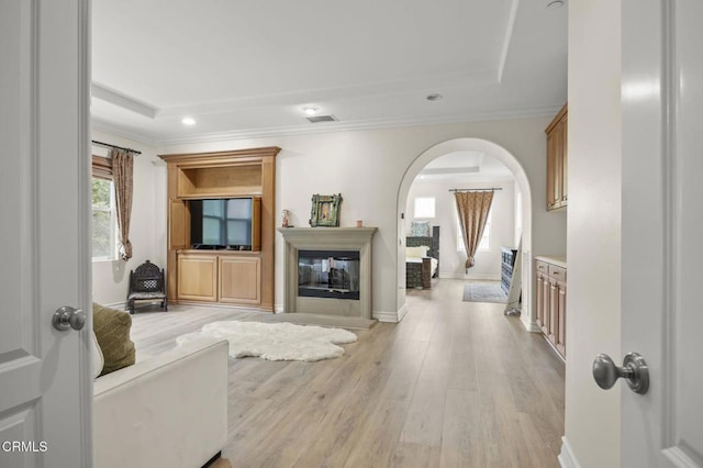 living room with light wood finished floors, crown molding, visible vents, a raised ceiling, and arched walkways