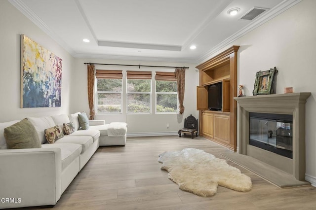 living room with light wood finished floors, crown molding, visible vents, baseboards, and a glass covered fireplace