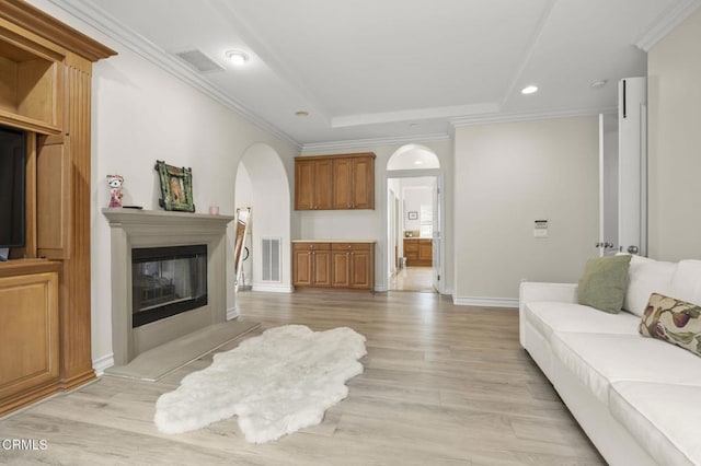 living area featuring a tray ceiling, visible vents, arched walkways, a glass covered fireplace, and recessed lighting