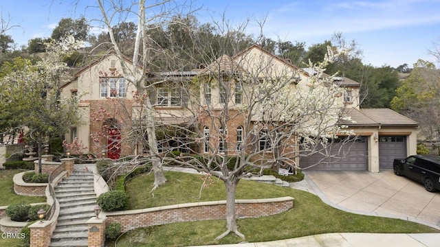 tudor home featuring a front yard, an attached garage, stucco siding, and driveway