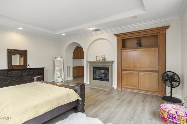 bedroom featuring a tray ceiling, crown molding, light wood-type flooring, visible vents, and recessed lighting