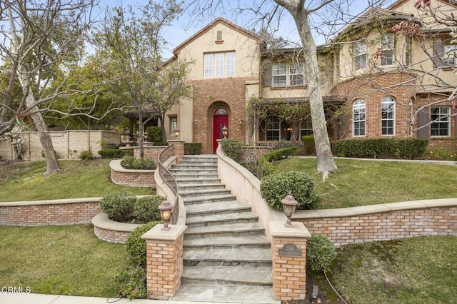 view of front of house featuring stucco siding, brick siding, and a front yard