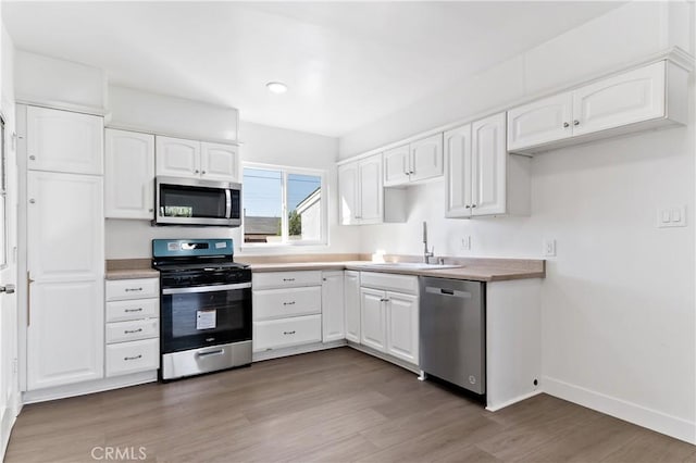 kitchen featuring baseboards, light wood-style flooring, stainless steel appliances, white cabinetry, and a sink