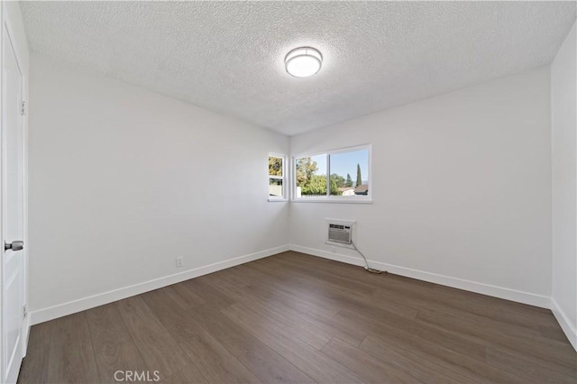 unfurnished room with a wall mounted air conditioner, baseboards, a textured ceiling, and dark wood-style floors