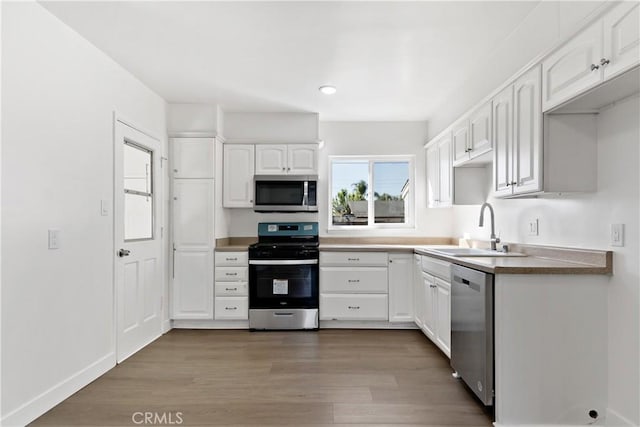 kitchen featuring baseboards, dark wood-style floors, white cabinets, stainless steel appliances, and a sink