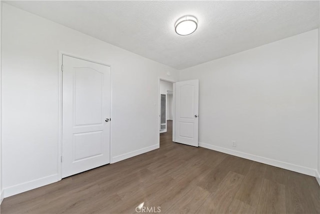 unfurnished bedroom featuring a textured ceiling, baseboards, and wood finished floors