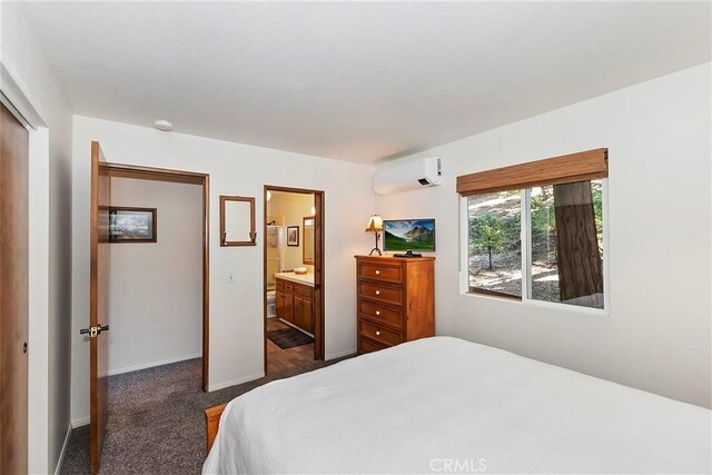 bedroom with baseboards, dark carpet, a wall unit AC, ensuite bathroom, and a closet