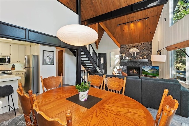 dining room with stairway, beamed ceiling, a fireplace, wood finished floors, and high vaulted ceiling