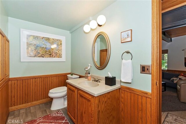 bathroom featuring vanity, toilet, a wainscoted wall, and wood walls