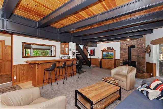 living room featuring a healthy amount of sunlight, beamed ceiling, stairway, wainscoting, and a wood stove