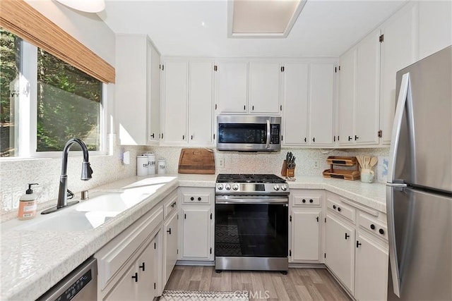 kitchen with a sink, stainless steel appliances, tasteful backsplash, and white cabinetry