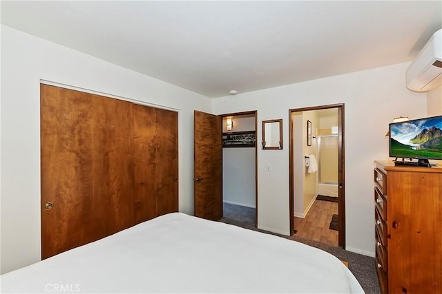 bedroom featuring ensuite bathroom, a wall mounted AC, a closet, dark colored carpet, and baseboards