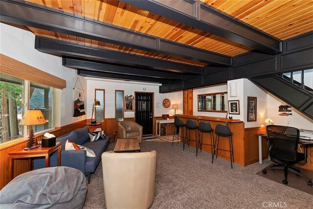 carpeted living room featuring beamed ceiling, wooden walls, a bar, wainscoting, and wood ceiling