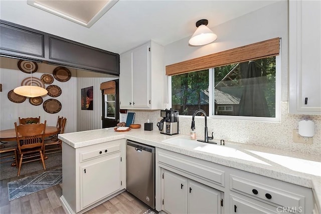 kitchen with a sink, stainless steel dishwasher, light countertops, and light wood finished floors