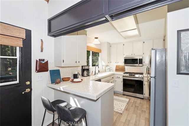 kitchen with decorative backsplash, appliances with stainless steel finishes, white cabinetry, and a peninsula