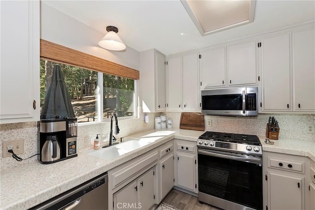 kitchen with tasteful backsplash, light countertops, stainless steel appliances, white cabinetry, and a sink