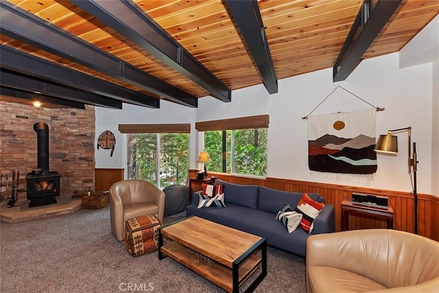 carpeted living area with wooden walls, beam ceiling, a wood stove, wood ceiling, and wainscoting