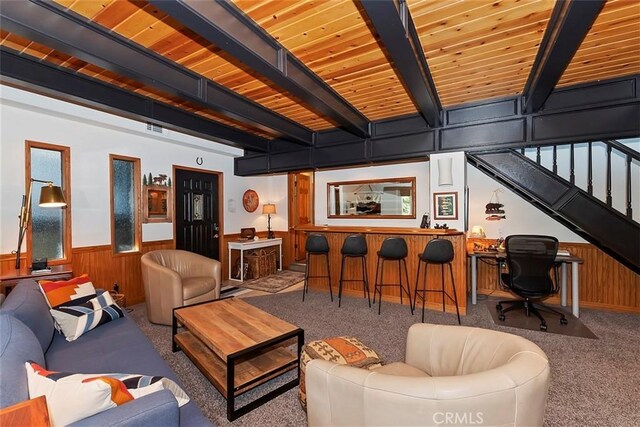 carpeted living room featuring beamed ceiling, a wainscoted wall, stairway, wooden ceiling, and wood walls