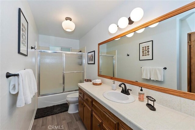 full bathroom featuring bath / shower combo with glass door, toilet, wood finished floors, and vanity