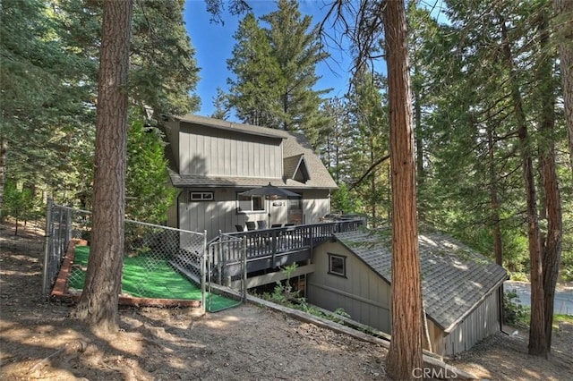 back of house featuring roof with shingles, a deck, and fence