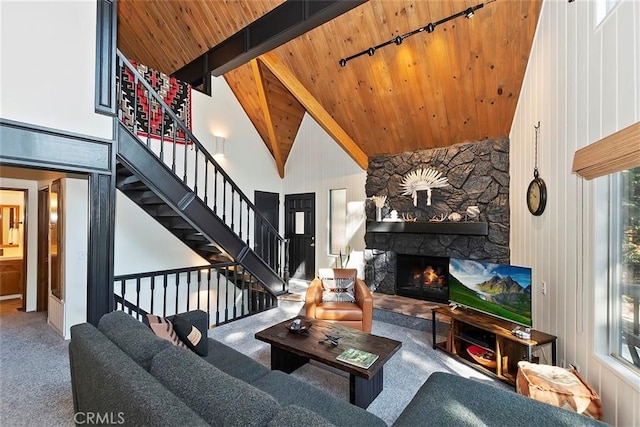 living area with beamed ceiling, stairway, carpet floors, a stone fireplace, and wooden ceiling