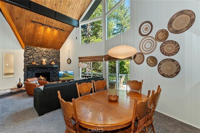 dining room with carpet, high vaulted ceiling, beam ceiling, a stone fireplace, and wood ceiling