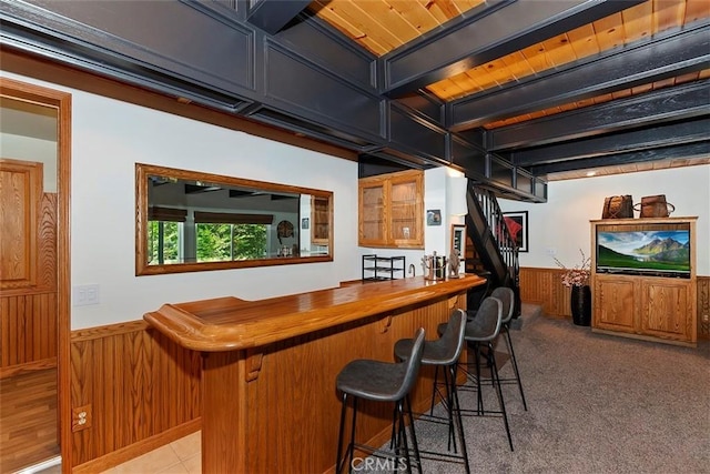 bar with wooden walls, beamed ceiling, a wainscoted wall, light colored carpet, and a dry bar