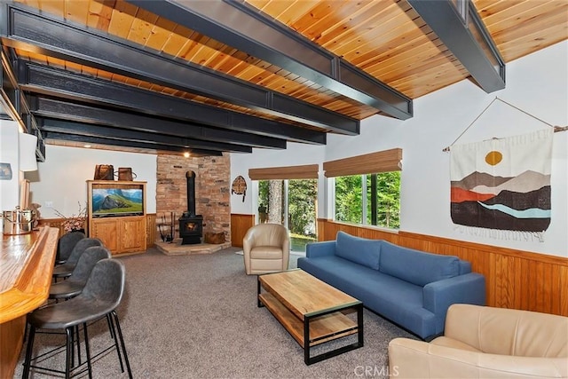 living area featuring beamed ceiling, carpet flooring, wainscoting, wooden ceiling, and a wood stove