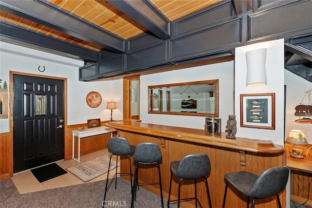 bar with carpet, a wainscoted wall, beam ceiling, wooden ceiling, and tile patterned floors