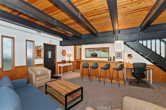living room with beam ceiling, stairway, wooden walls, carpet flooring, and wainscoting