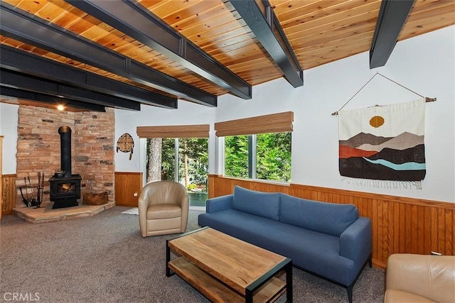 carpeted living area with wood walls, beam ceiling, wainscoting, wooden ceiling, and a wood stove