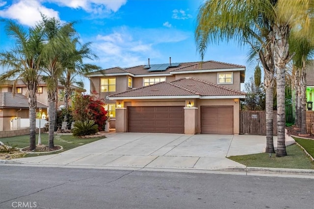 view of front of house featuring stucco siding, driveway, roof mounted solar panels, fence, and an attached garage