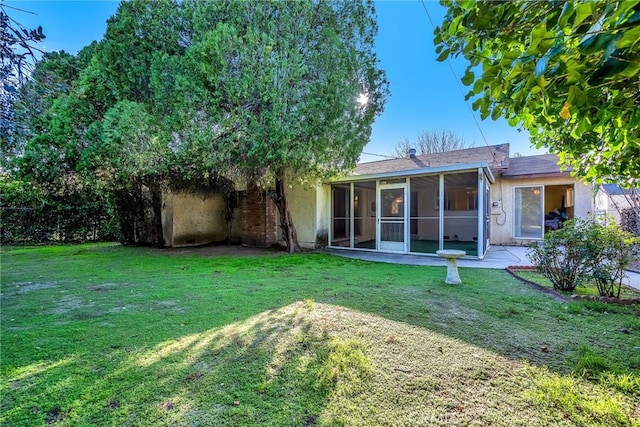 rear view of property with a lawn, a sunroom, and stucco siding