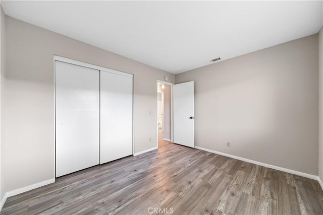 unfurnished bedroom featuring a closet, visible vents, baseboards, and wood finished floors