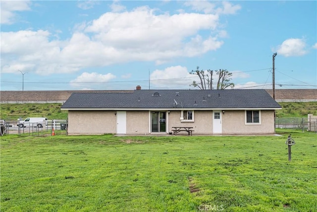 rear view of house with a yard, stucco siding, and fence