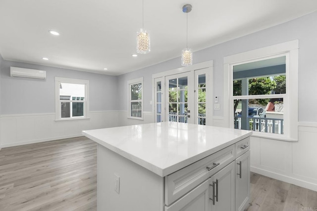 kitchen featuring wainscoting, light wood finished floors, a wall mounted air conditioner, light countertops, and decorative light fixtures