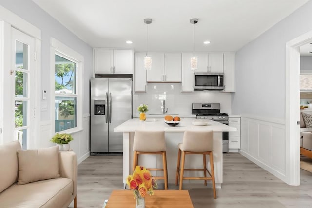 kitchen featuring backsplash, stainless steel appliances, white cabinetry, and light wood finished floors