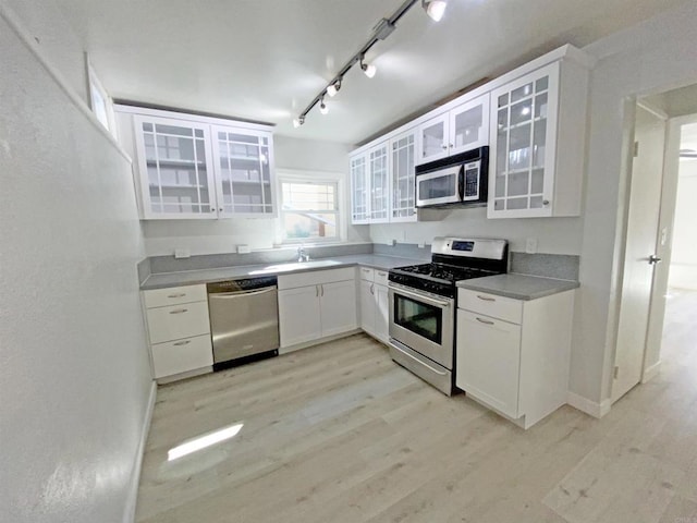 kitchen featuring track lighting, white cabinetry, a sink, light wood finished floors, and stainless steel appliances