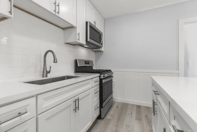 kitchen featuring decorative backsplash, white cabinetry, a sink, stainless steel appliances, and light wood-style flooring