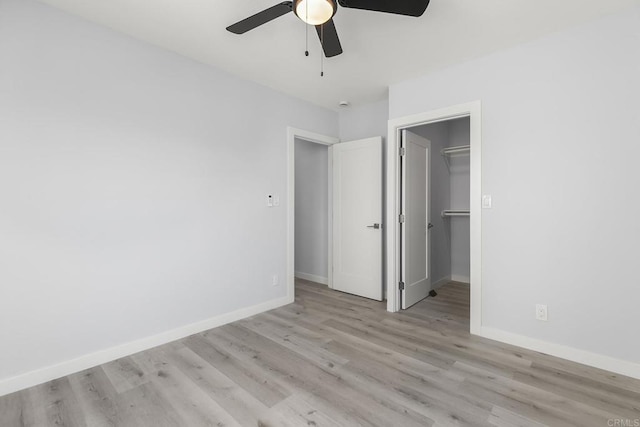 unfurnished bedroom featuring a closet, baseboards, light wood-type flooring, a spacious closet, and a ceiling fan