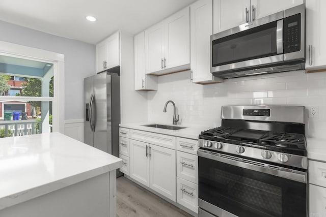 kitchen with a sink, appliances with stainless steel finishes, white cabinetry, and light countertops