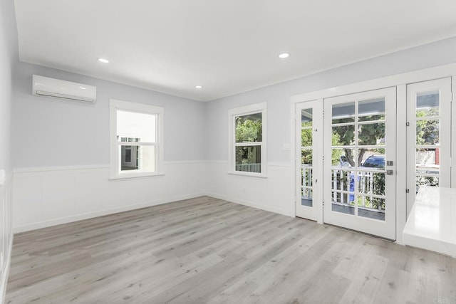 unfurnished room featuring wood finished floors, a wall unit AC, a wealth of natural light, and a wainscoted wall