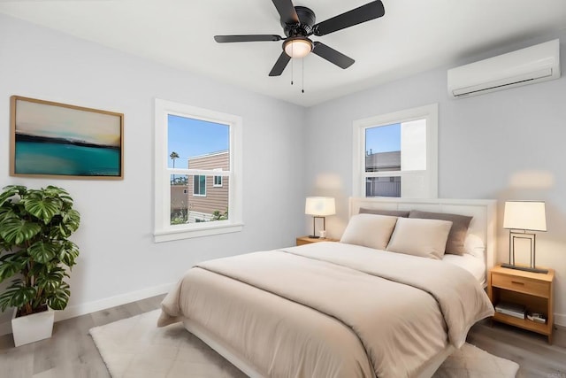 bedroom with wood finished floors, baseboards, ceiling fan, and a wall unit AC
