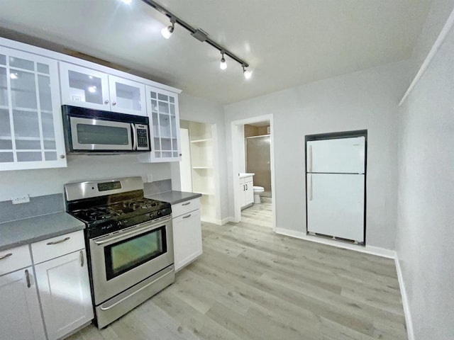 kitchen featuring track lighting, freestanding refrigerator, stainless steel gas stove, light wood-type flooring, and white cabinetry