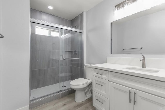 bathroom featuring vanity, a stall shower, toilet, and wood finished floors