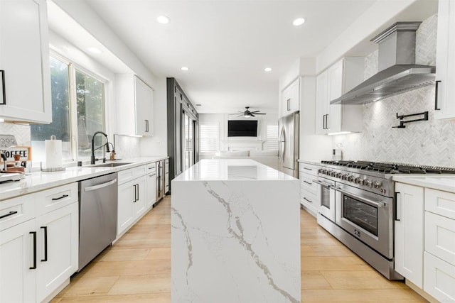 kitchen with a kitchen island, light wood-style flooring, a sink, stainless steel appliances, and wall chimney range hood