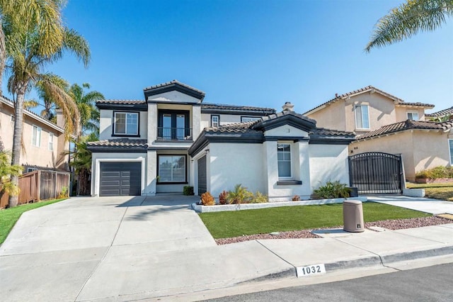 mediterranean / spanish house with stucco siding, a gate, fence, concrete driveway, and a tiled roof