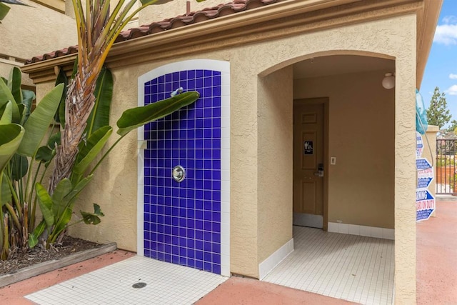 view of exterior entry with stucco siding and a tile roof